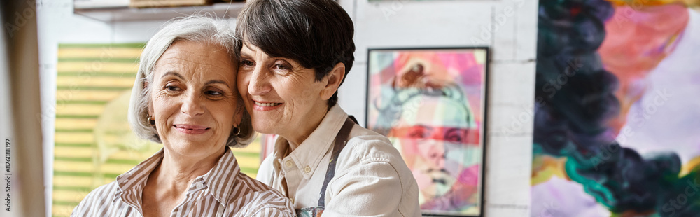 Two women stand together in an art studio. Two women stand together in an art studio.