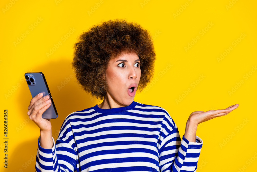 Portrait of pretty young woman hold smart phone empty space wear striped shirt isolated on yellow color background
