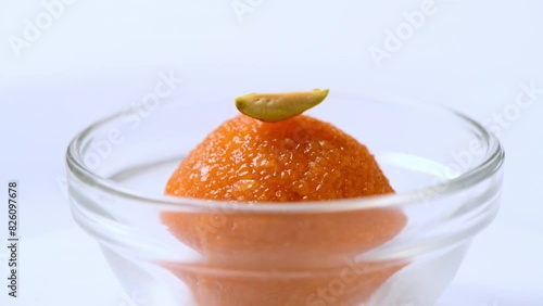 Delicious looking Motichur ladoo (motichoor) in a glass bowl. Closeup front shot of motichur laddoo rotating slowly against white . Yummy looking indian sweet . Ladoo with pistachio topping. photo