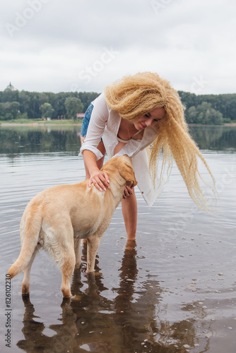 Young woman playing with her labrador retriever dog in river.