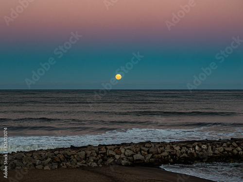Full Moon Rising Over Ocean Horizon at Rocky Beach During Dusk