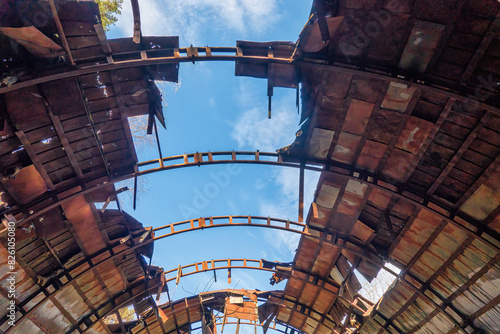 Inside view of the destroyed metal roof of an old semicircular hangar. Sheets of iron, structural elements and blue sky are visible. Background. Grunge.