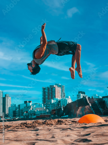Man Performing Backflip at Beachfront With Urban Skyline Midday