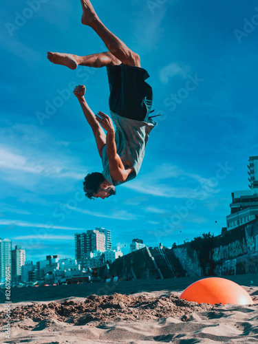 Man Performing Backflip at Beachfront With Urban Skyline Midday