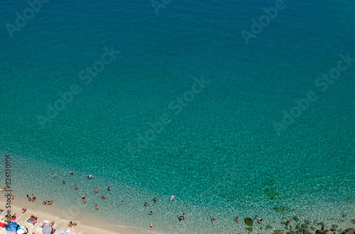 Aerial view of sandy beach with swimming people in sea with transparent blue water in summer. © Alekss