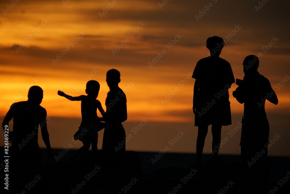 Fototapeta premium Silhouette of a group of local Papua people enjoying sunset at the beach.