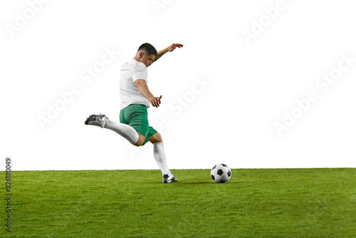 Side view of young fit man, soccer player ready to kick a soccer ball on green grass field against white background. Concept of professionals sport, competition, tournament, energy, action. Ad © Lustre