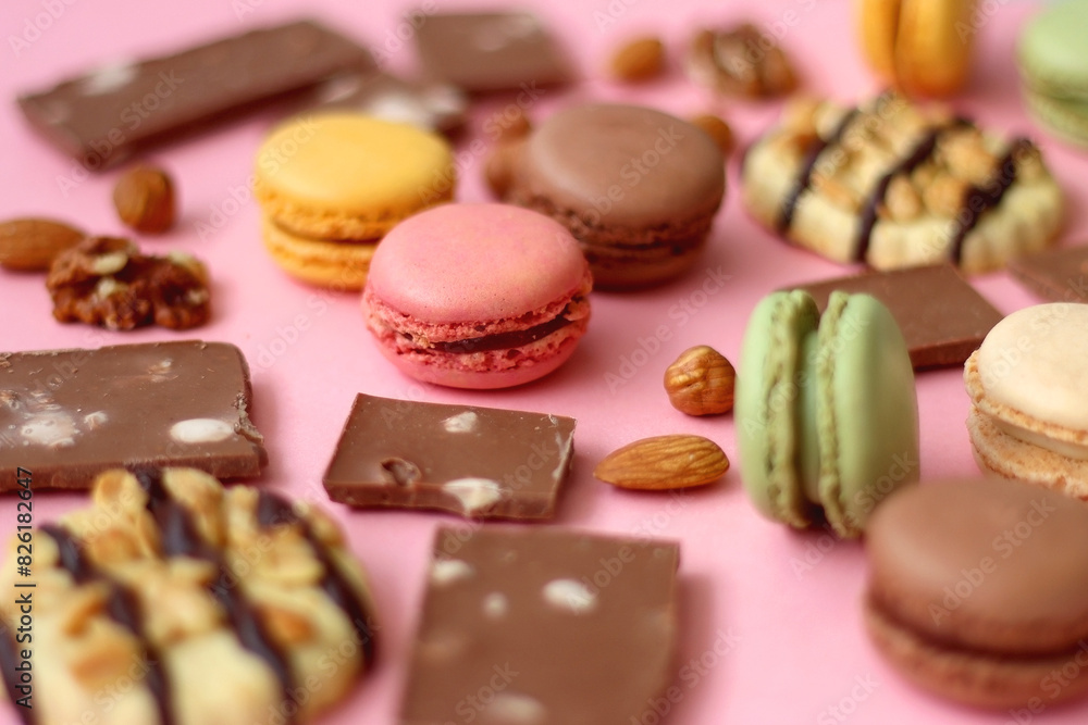 Pastel macarons, almond chocolate, peanut butter cookies and various nuts on bright pink background. Selective focus. Pastel macarons, almond chocolate, peanut butter cookies and various nuts on bright pink background. Selective focus.
