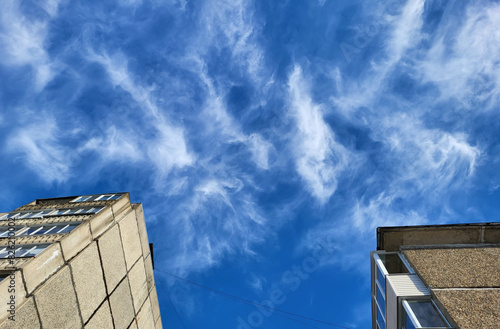 Blue sky with fluffy feathery clouds and the edge of the facade of a multi-storey building building