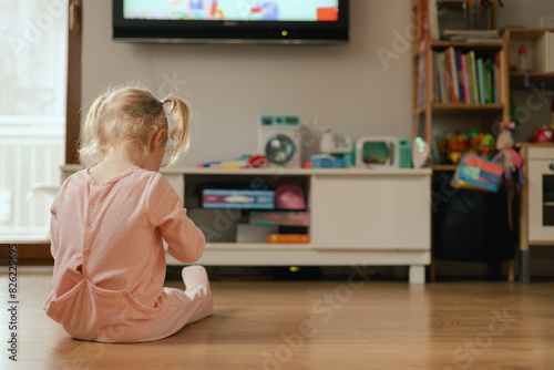 Portrait of happy baby playing with toys and watches cartoons on TV in playroom. Children and technology concept. Alpha Generation and modern technology with electronic device. Part of the series photo