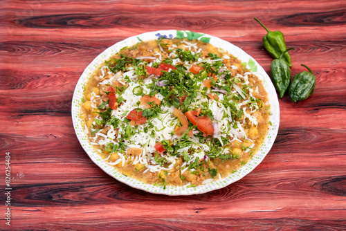 Spicy Naga Chotpoti with green pepper include chickpea, tomato, onion, cabbage, chilli, coriander, and sauce served in plate isolated on wooden table side view of bangladeshi street food