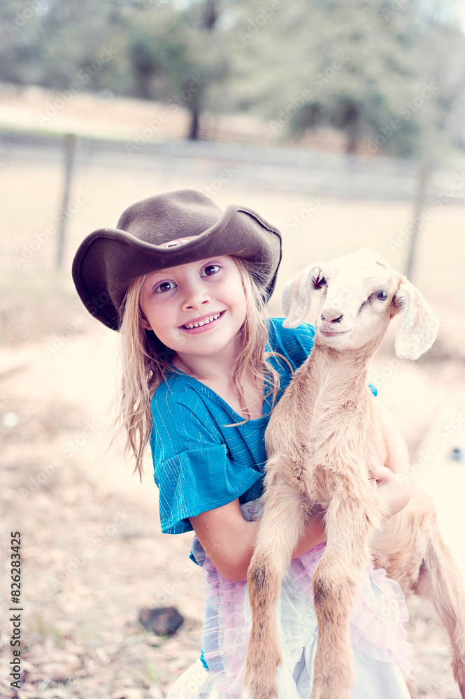 Smiling girl in cowboy hat holding a young goat outdoors. Smiling girl in cowboy hat holding a young goat outdoors.