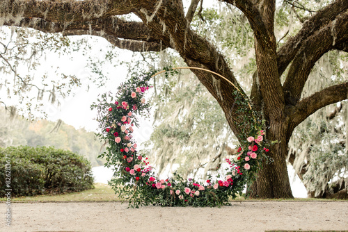 Circular floral arrangement with pink and red flowers under oak tree
