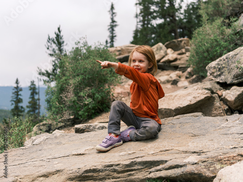 Child sitting on a rock pointing in the distance during a hike