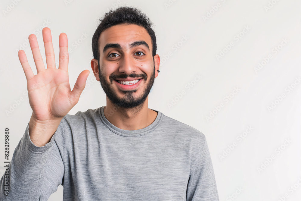 Cheerful Middle Eastern Man in Grey Shirt Waving Hello with a Friendly Smile Cheerful Middle Eastern Man in Grey Shirt Waving Hello with a Friendly Smile