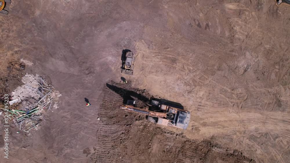 Top-view shot of an excavator removing dirt, with a small tractor with loader positioned next to it. Top-view shot of an excavator removing dirt, with a small tractor with loader positioned next to it.