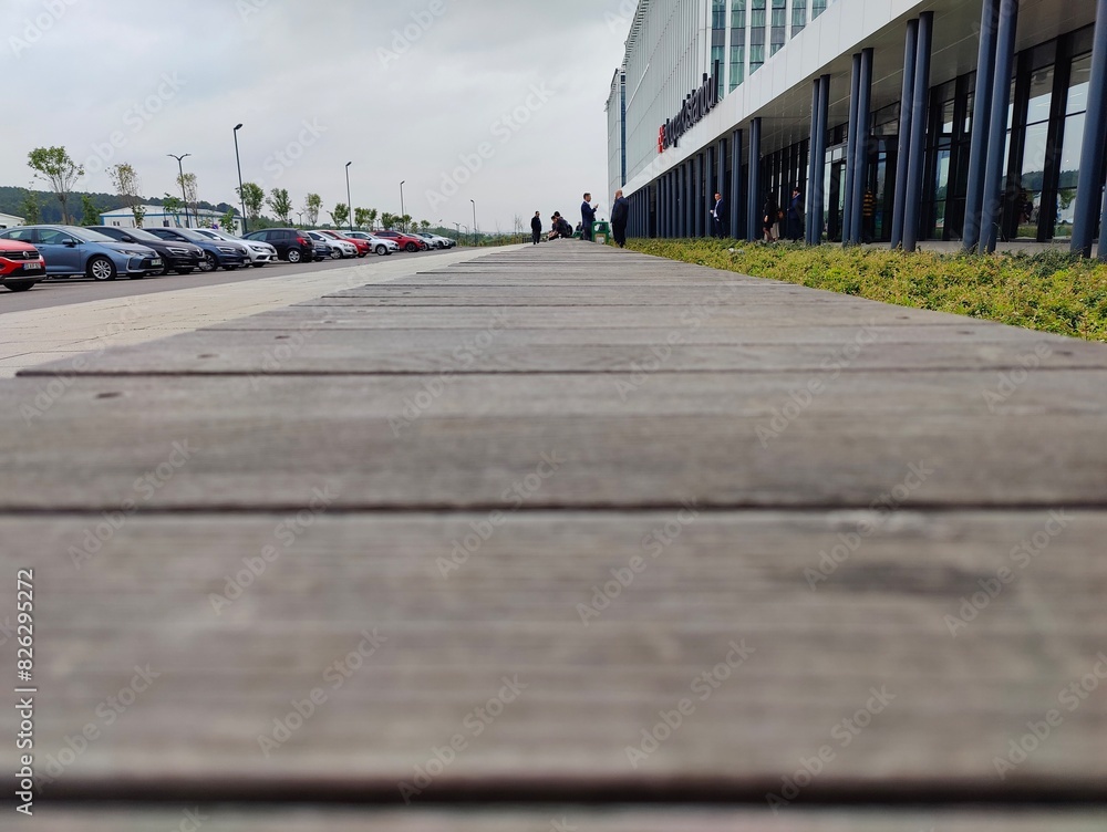 Obraz premium Wooden Boardwalk with Well-Maintained Planks in a Pedestrian-Friendly Outdoor Setting Adjacent to Parking Area