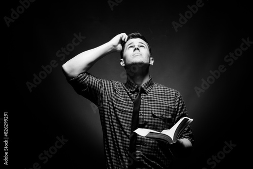 Well dressed man holding a Bible and looking up at God in confusion in grayscale photo