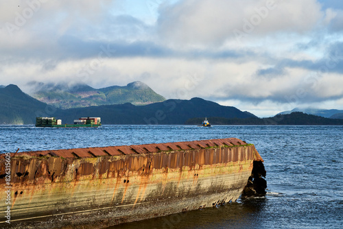 View over a rusty breakwater of a tug and barge traveling down an ocean passage on a bright day. photo