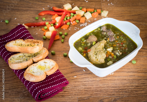 Aguadito de pollo is a traditional Peruvian soup prepared with chicken, aji amarillo peppers, peas, corn, onions, potatoes, rice, and cilantro closeup on the bowl on the wooden table. Vertical photo