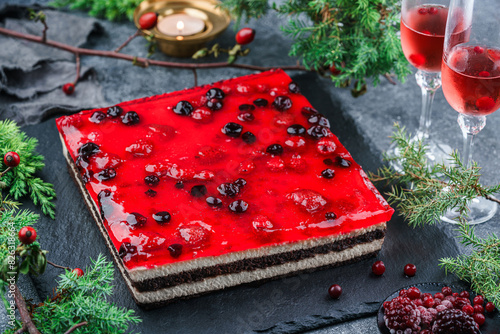 Layer creamy mousse cake with berry jelly on grey background with glasses of wine, berries, candles and fir banches. Sweets, dessert and pastry, top view, close up photo