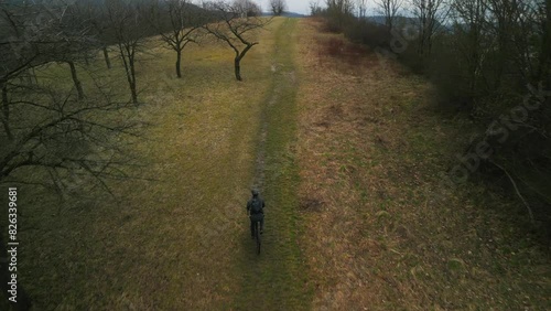 Drone footage of a cyclist riding up the hill surrounded by leafless trees during autumn in Germany photo