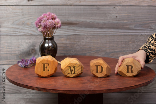 Letters EMDR written on irregular wooden blocks. A woman's hand adds the last block, Eye Movement Desensitization and Reprocessing psychotherapy treatment concept.