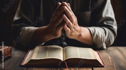 Focus on hands clasped in prayer over an open book, suggesting study or devotion