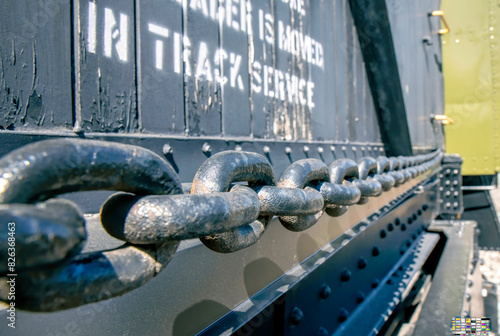 A long metal chain hanging on the side of an old blue wooden railcar, sunshine, nobody