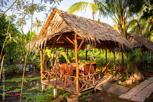 Wooden gazebo with palm tree leaves roof in tropical forest © Maresol