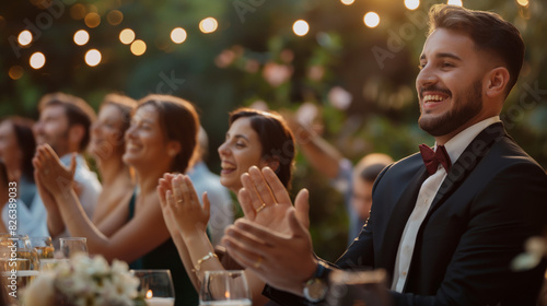 A smartly dressed man clapping with a smile at a well-lit outdoor evening celebration photo