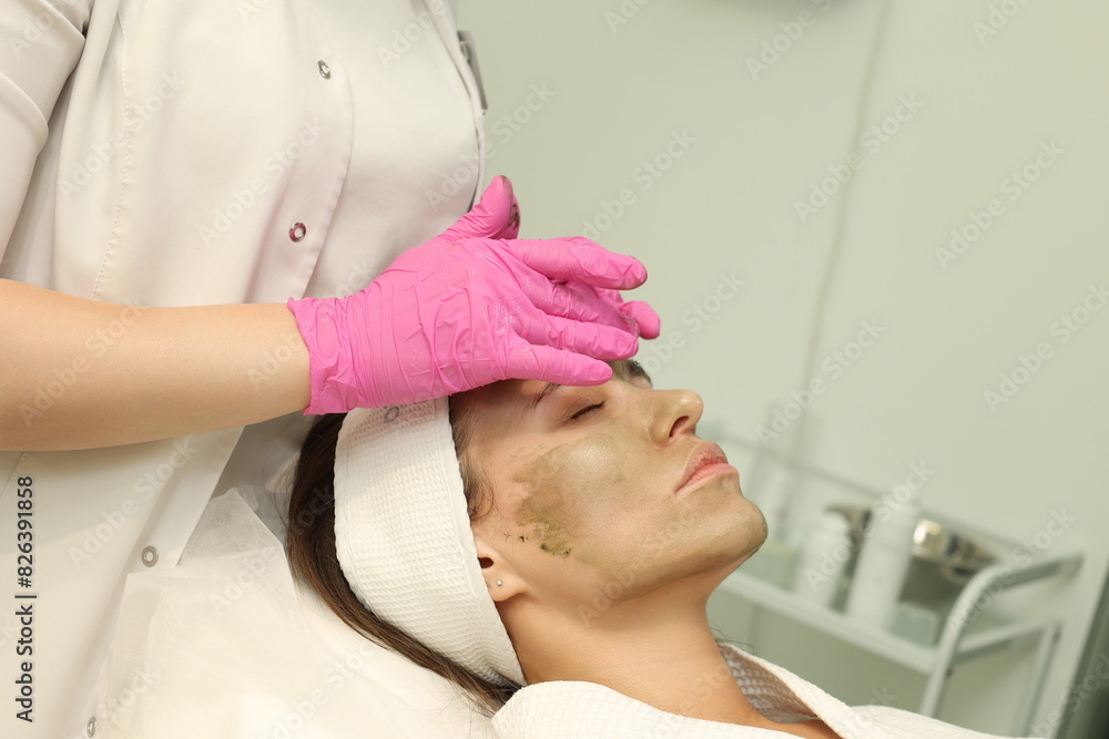Woman in cosmetologyst's cabinet. The office of a beautician applying a mask to a woman's face in a spa salon, view above. Aesthetic procedure. Care mask for facial skin. Face massage Woman in cosmetologyst's cabinet. The office of a beautician applying a mask to a woman's face in a spa salon, view above. Aesthetic procedure. Care mask for facial skin. Face massage