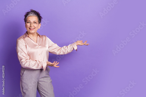 Photo portrait of lovely senior lady point hold hands empty space dressed stylish satin garment isolated on violet color background