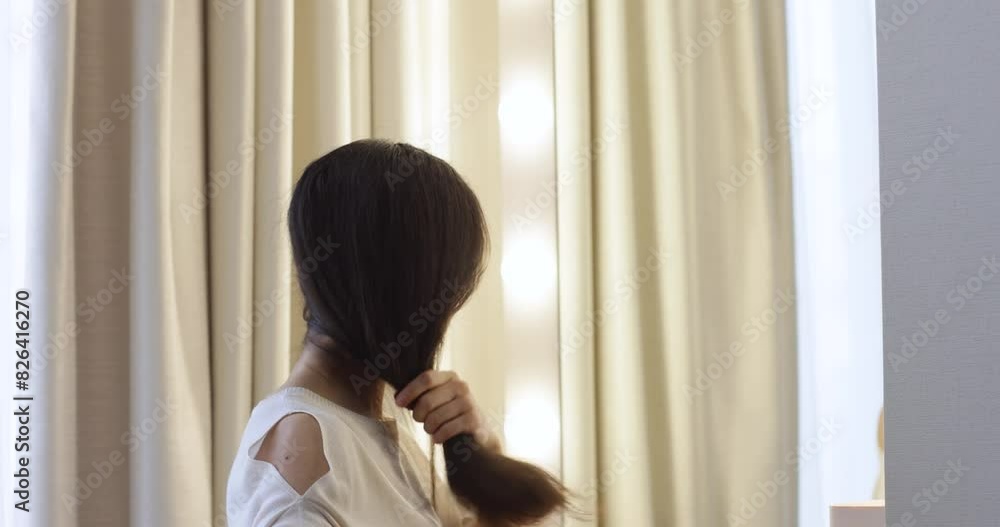 caucasian woman looking in mirror and combing long healthy straight hair in bedroom caucasian woman looking in mirror and combing long healthy straight hair in bedroom