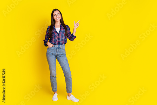 Full size photo of attractive young woman posing model point look empty space dressed plaid clothes isolated on yellow color background