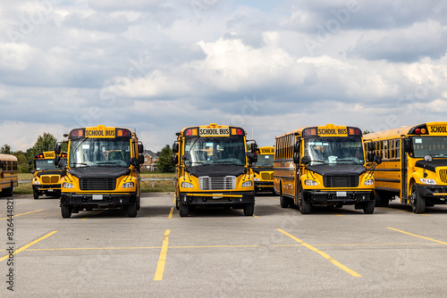 Yellow school buses lined up in an empty parking lot - under a partly cloudy sky. Taken in Toronto, Canada.