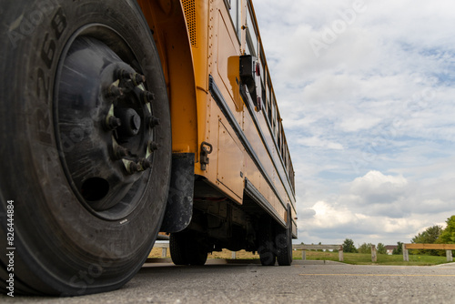 Low angle view of yellow school bus - detailed tire and body - cloudy sky backdrop. Taken in Toronto, Canada.