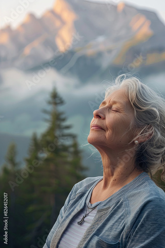 Senior woman doing breathing exercise in nature on early morning with fog and mountains in background
