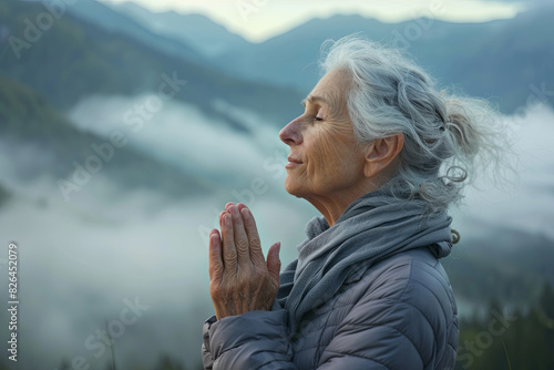 Senior woman doing breathing exercise in nature on early morning with fog and mountains in background
