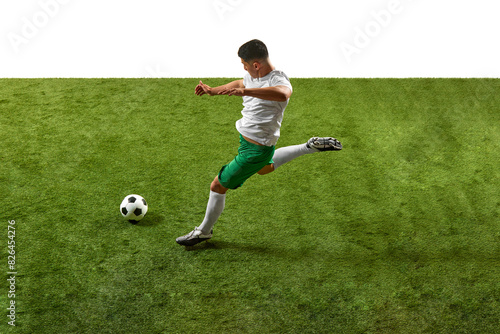 Action shot of young athletic guy, footballer in green and white gear, executing powerful kick on grassy pitch isolated white backdrop. Concept of professionals sport, competition, tournament, action. © Lustre