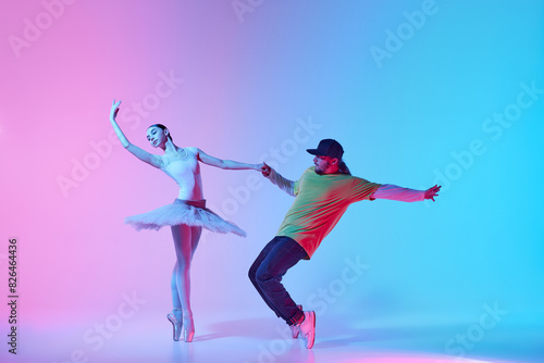 Tender young girl, beautiful ballerina dancing in tutu on pointe with energetic man, break dancer n gradient background in neon light. Concept of classical and modern dance, performance