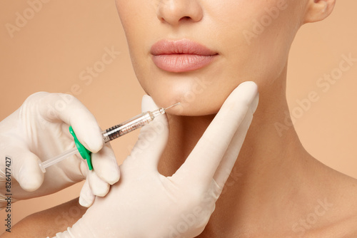 Quadro su tela Cosmetologist holding syringe near woman's chin, beauty injections with fillers