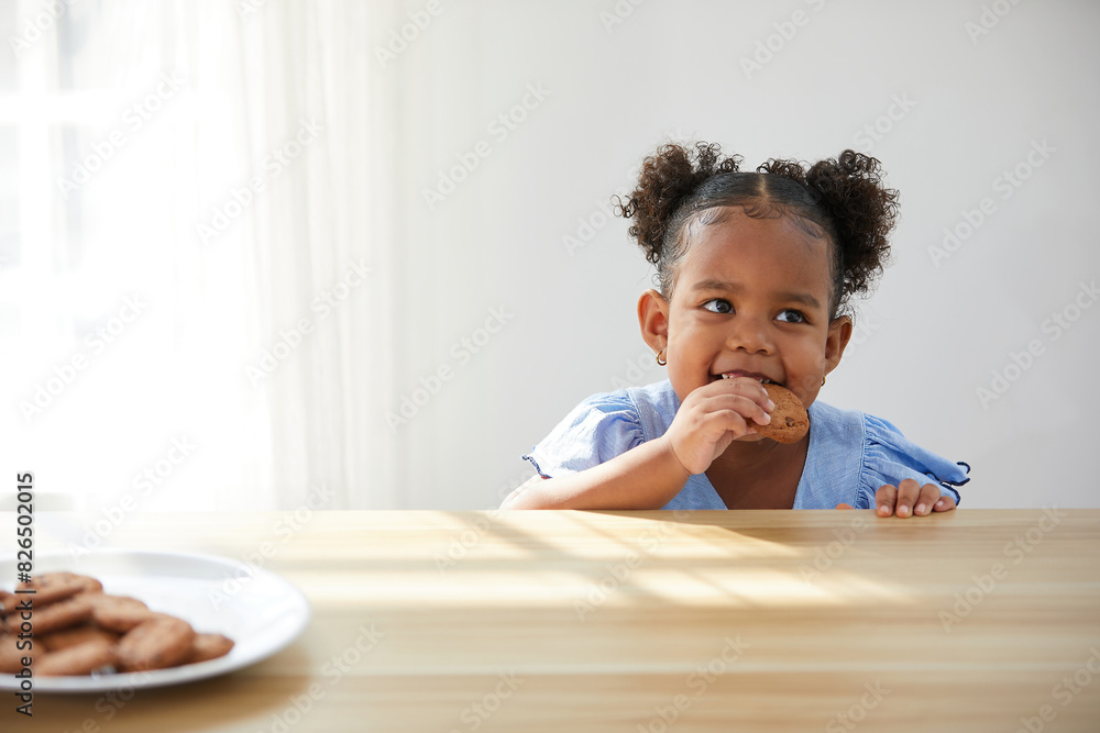 Fototapeta premium African child girl picking and eating chocolate cookies or biscuits from dish
