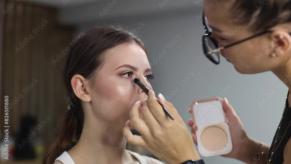 A handsome makeup artist applies paint with a brush and powder on the face under the eyes of a girl. A handsome makeup artist applies paint with a brush and powder on the face under the eyes of a girl.