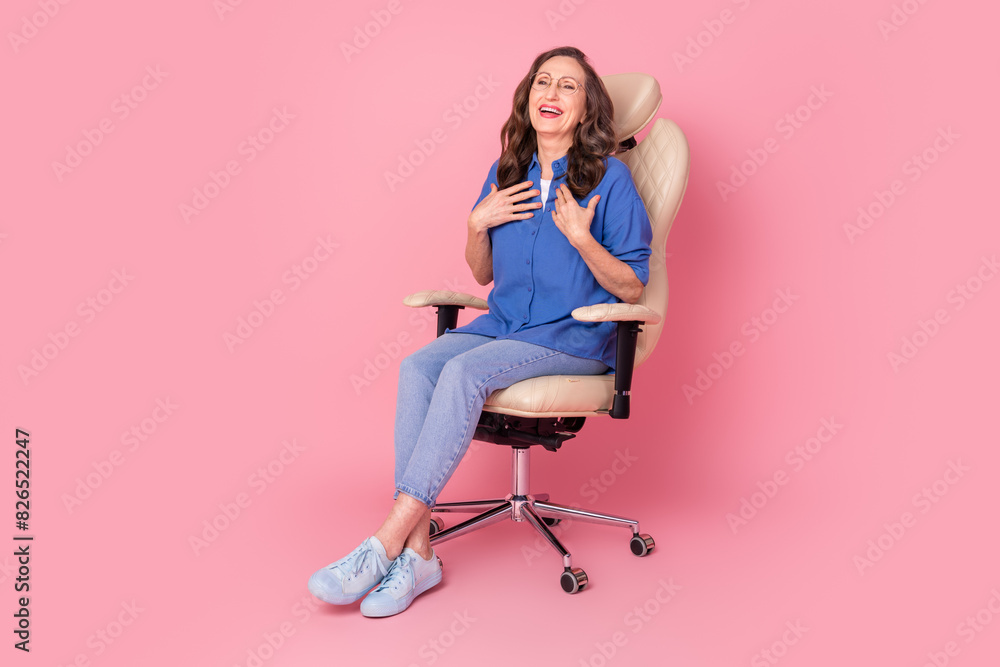 Full body photo of attractive retired woman sit armchair laugh dressed stylish blue clothes isolated on pink color background Full body photo of attractive retired woman sit armchair laugh dressed stylish blue clothes isolated on pink color background