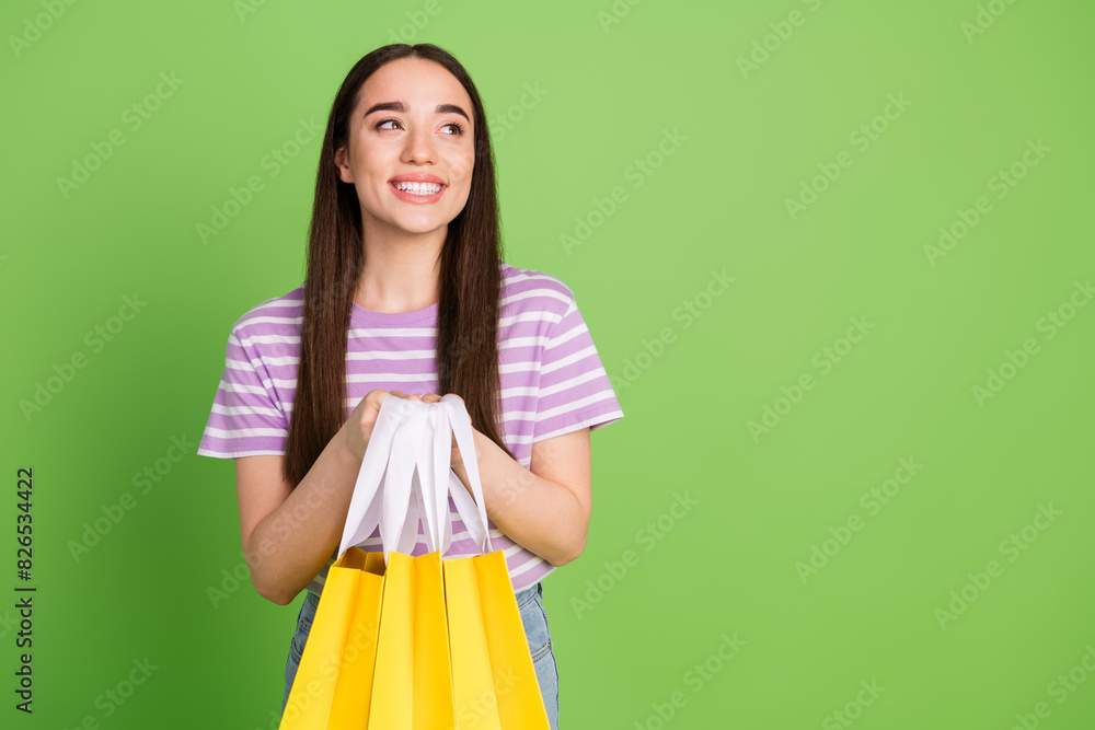 Photo of lovely young lady look empty space hold shopping bags dressed stylish striped violet garment isolated on green color background