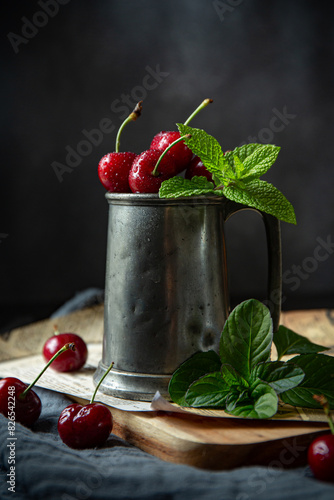 Fresh red cherries on in grey metal pot with green leaves of mint on newspaper's background 