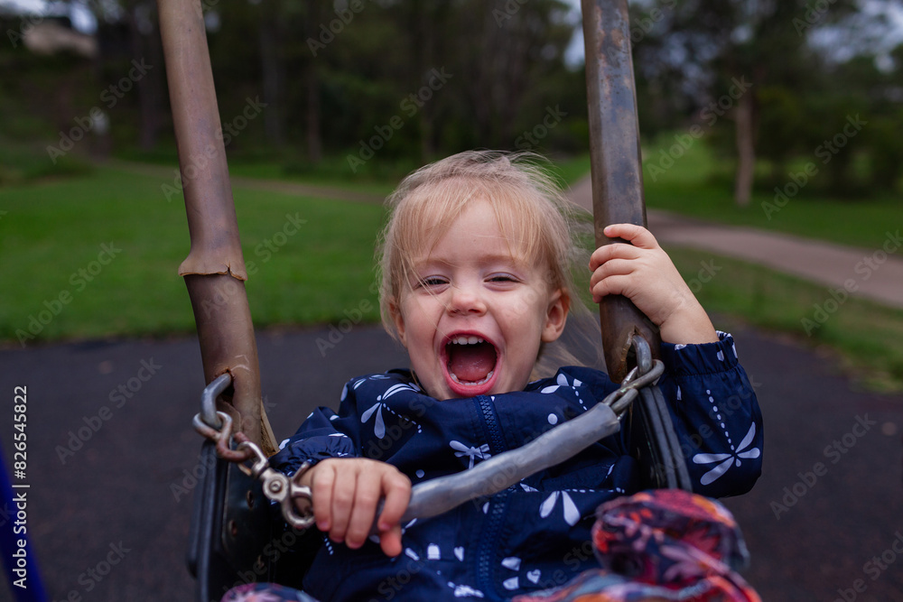 Little girl laughing in delight as she swings on park swing Little girl laughing in delight as she swings on park swing