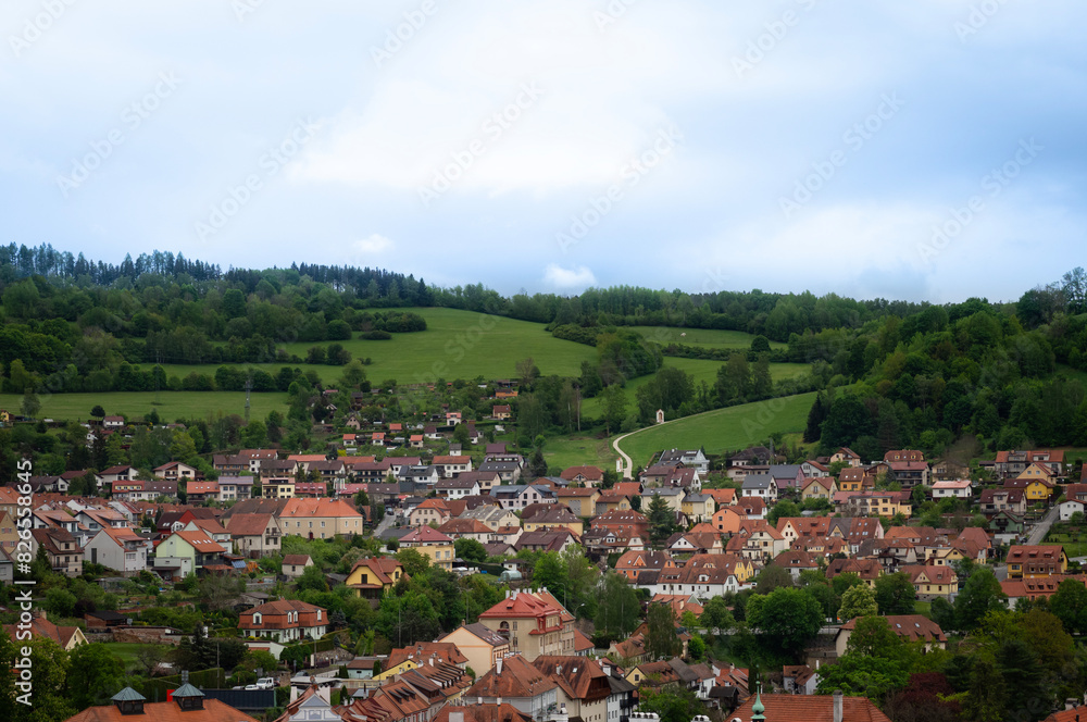 Cesky Krumlov cityscape and surrounding hills aerial panoramic view. Idyllic and peaceful life in spring time at small village with small green hill and bright sky background. Czech Republic