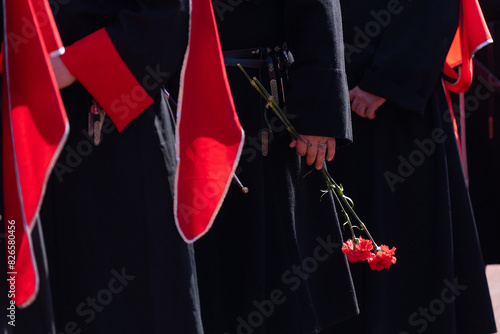 Cossacks in uniform lay flowers. Carnation flower in hand. A red carnation flower in the hands of a Cossack warrior. photo